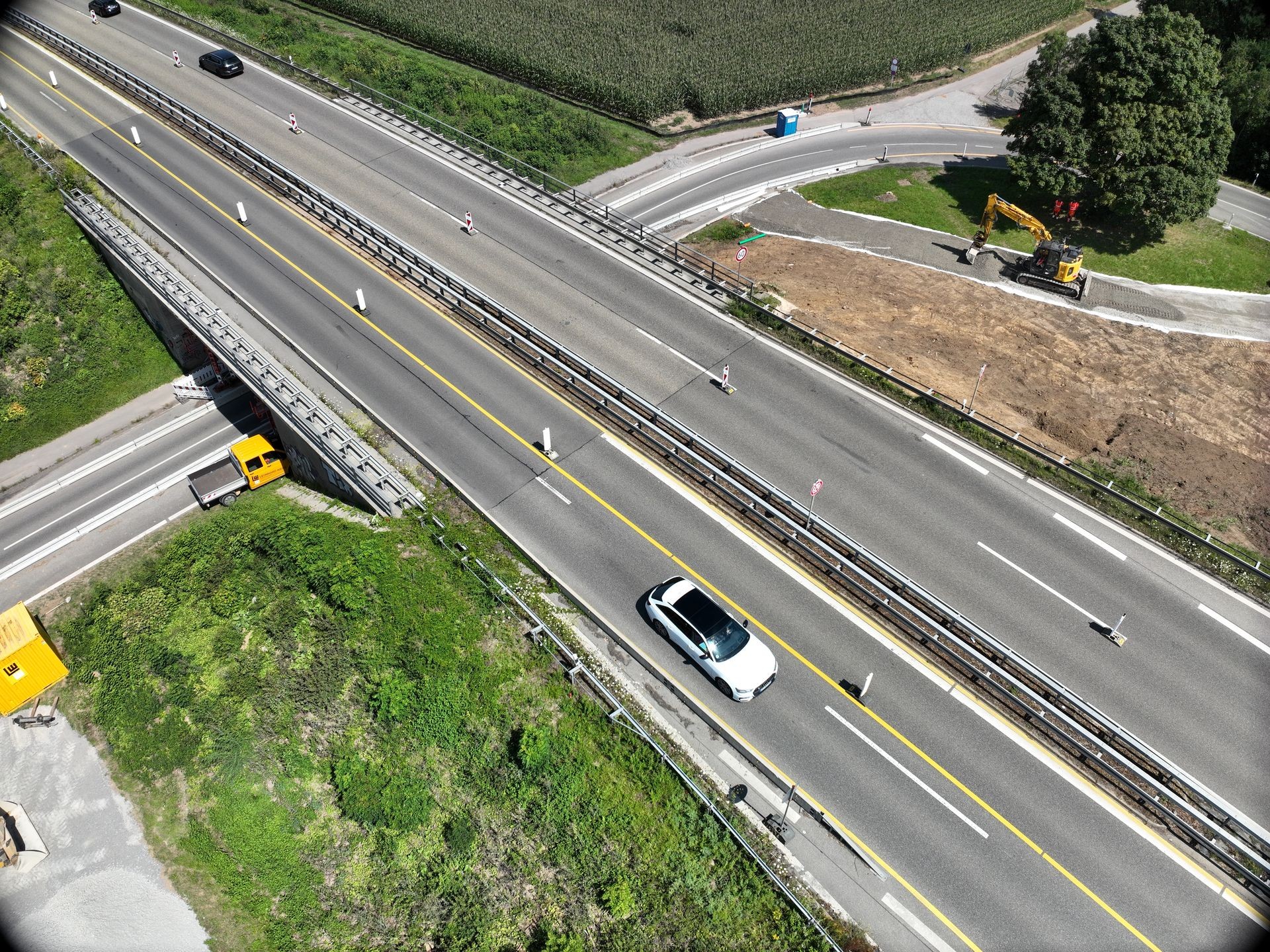 Aerial view of a highway with vehicles, construction site, and green surroundings.