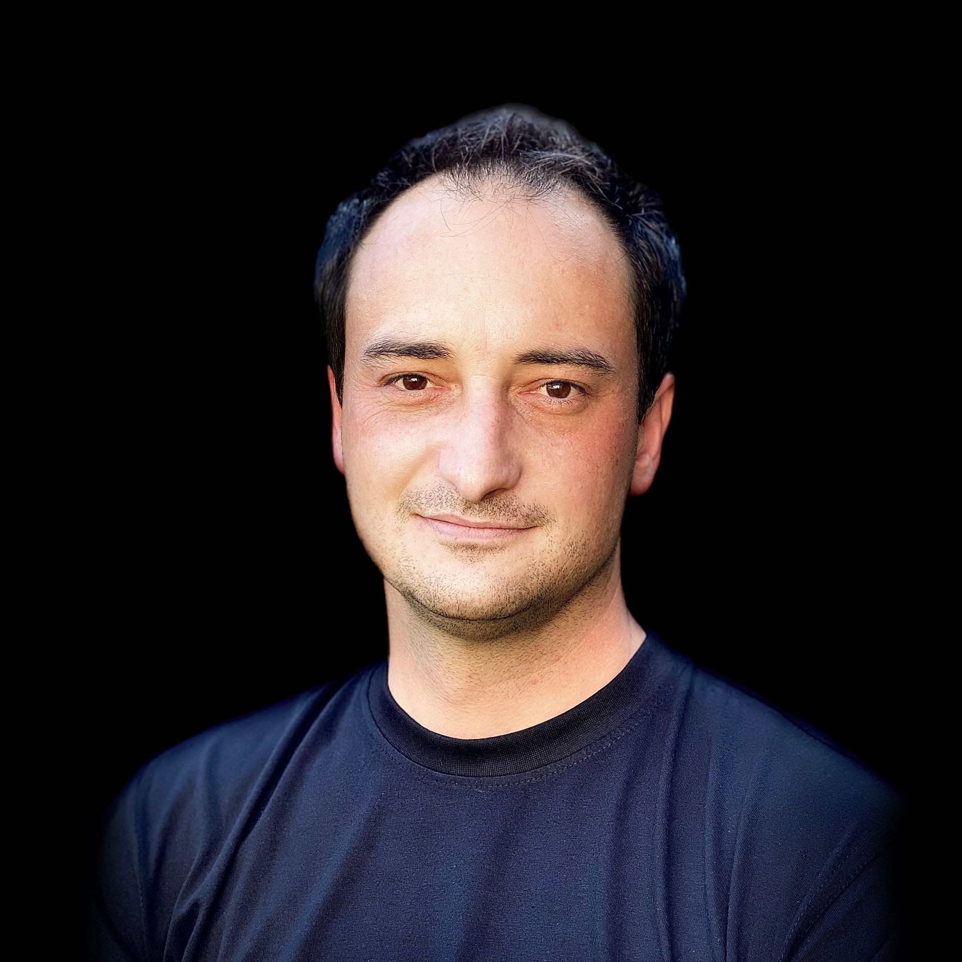 Person wearing a black crew-neck t-shirt, standing against a solid black background.